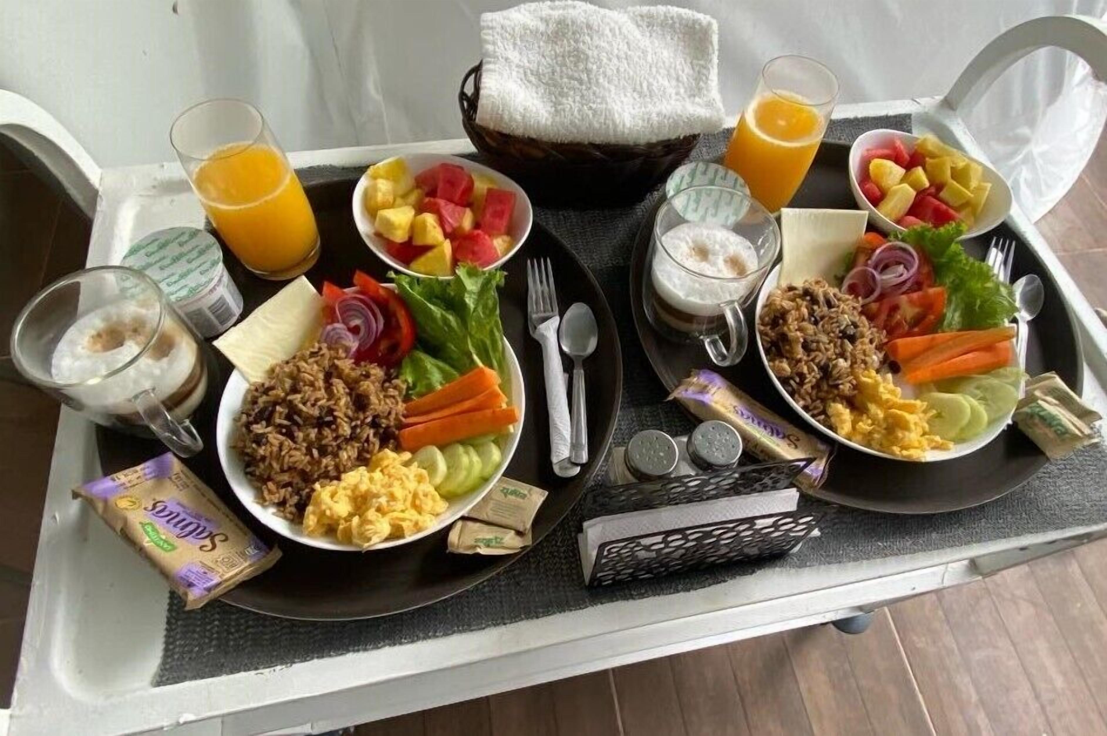 A breakfast tray with scrambled eggs, rice, vegetables, and fruit. There are also two glasses of orange juice and a bottle of milk.