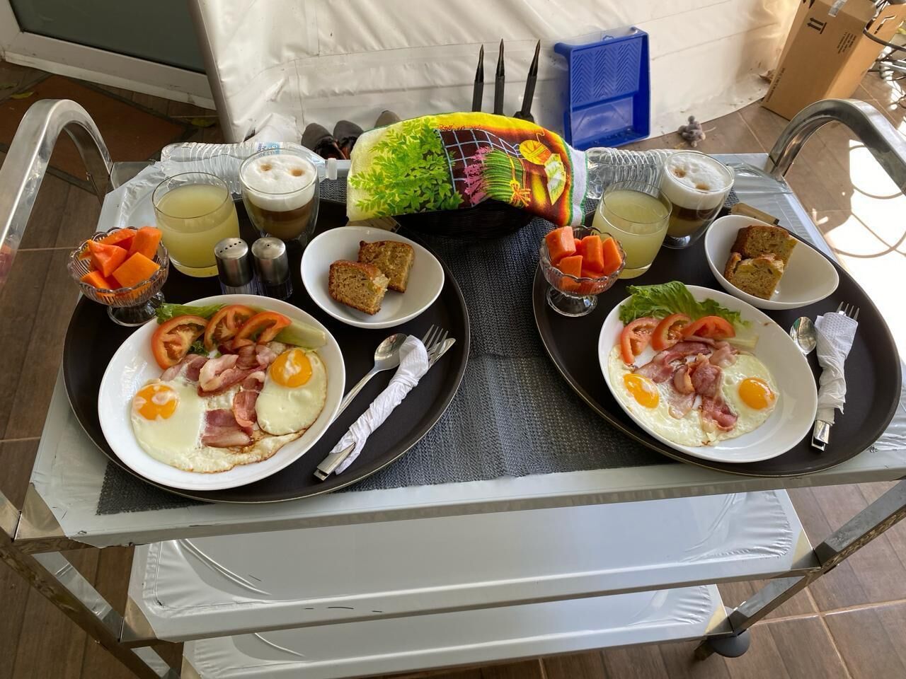 A breakfast tray with two plates of eggs, bacon, and tomatoes, accompanied by juice and toast.