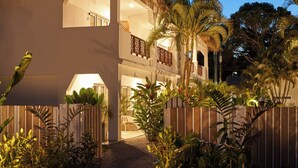 Un immeuble à plusieurs étages, doté d’un toit de chaume, entouré d’une végétation luxuriante et de palmiers.