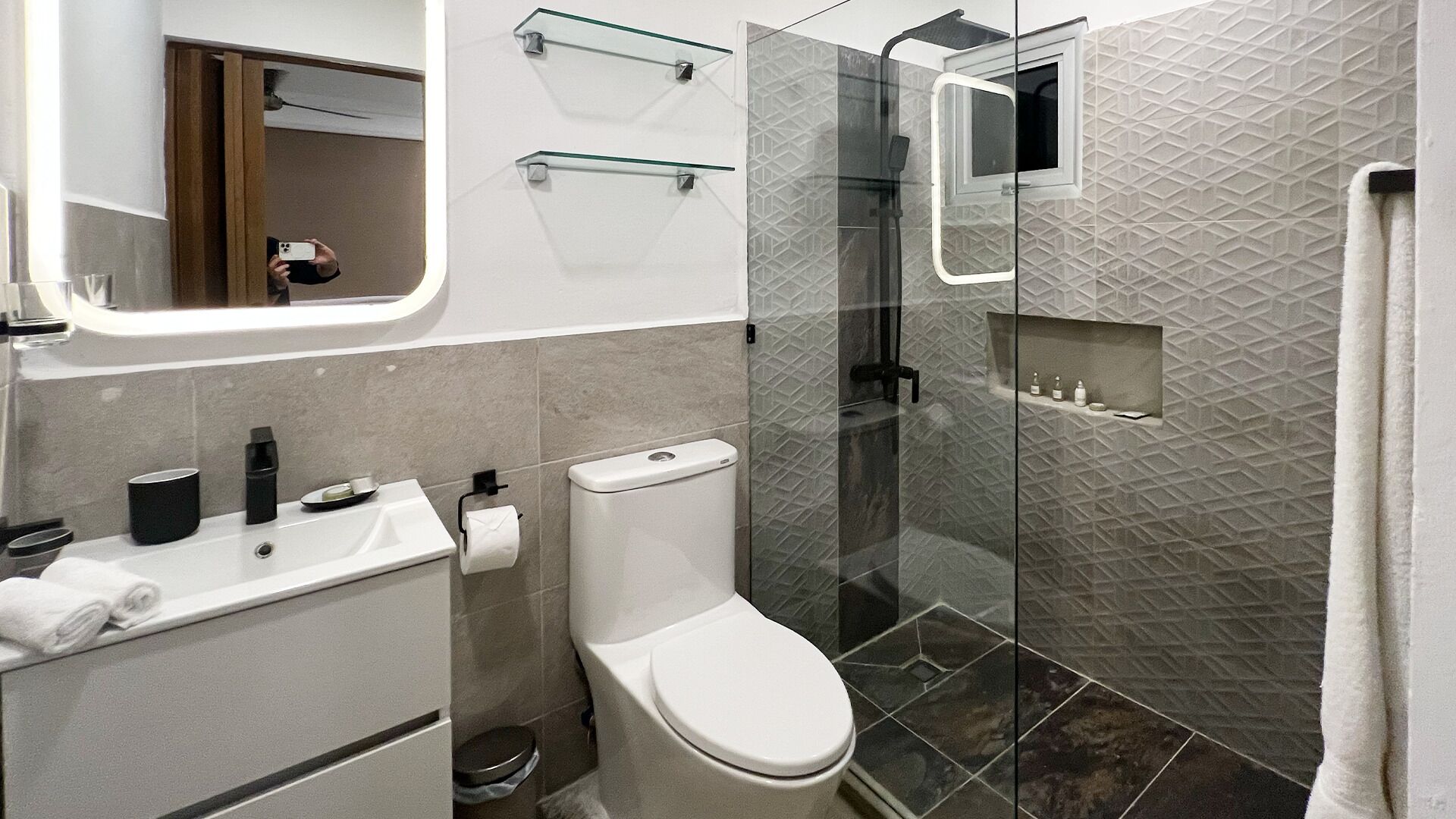 Un baño moderno con inodoro, lavamanos y cabina de ducha de vidrio.
