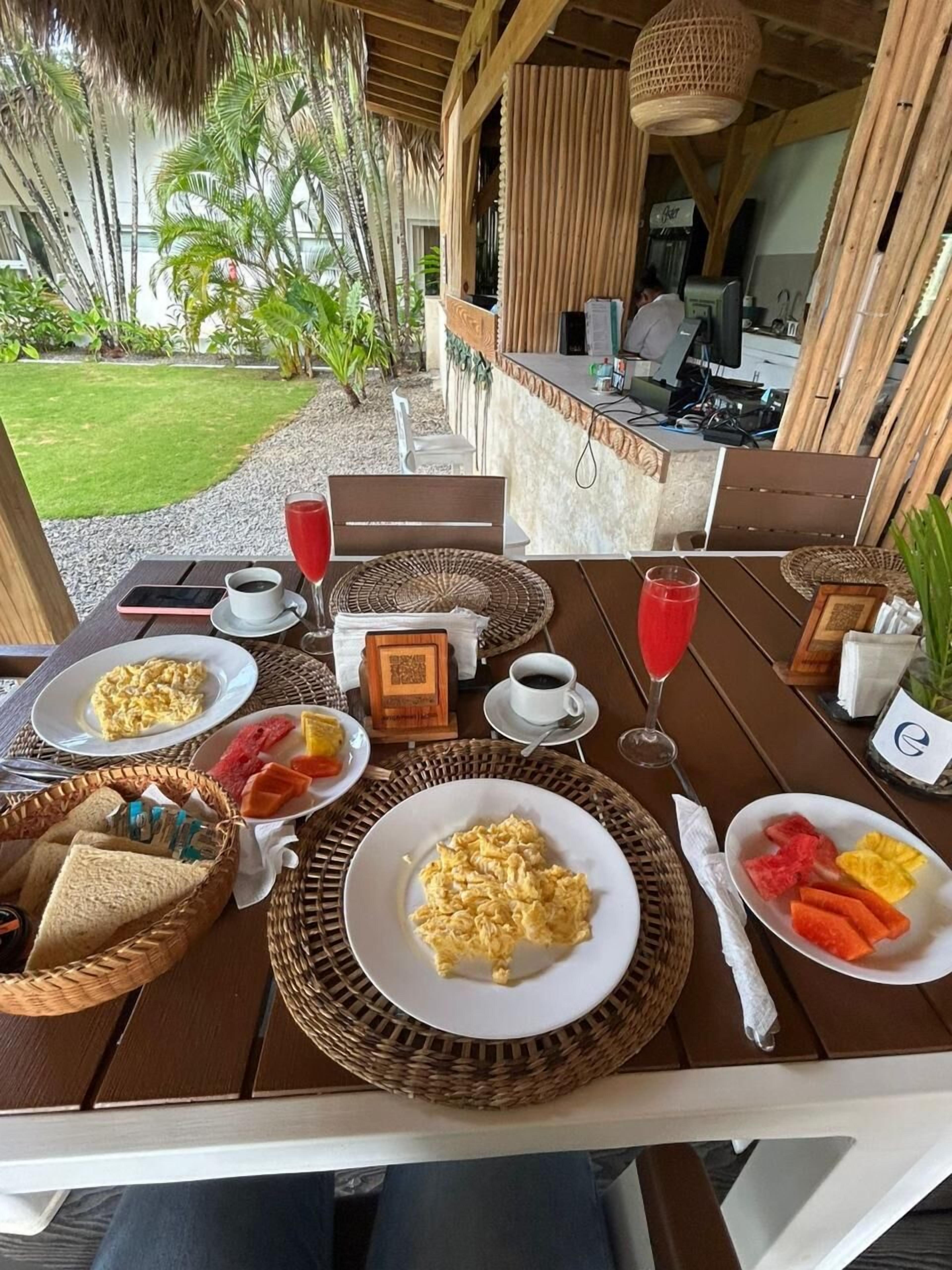 Una mesa lista para el desayuno, con platos de huevos revueltos, tostadas y fruta, una taza de café y un vaso de jugo de cerezas.