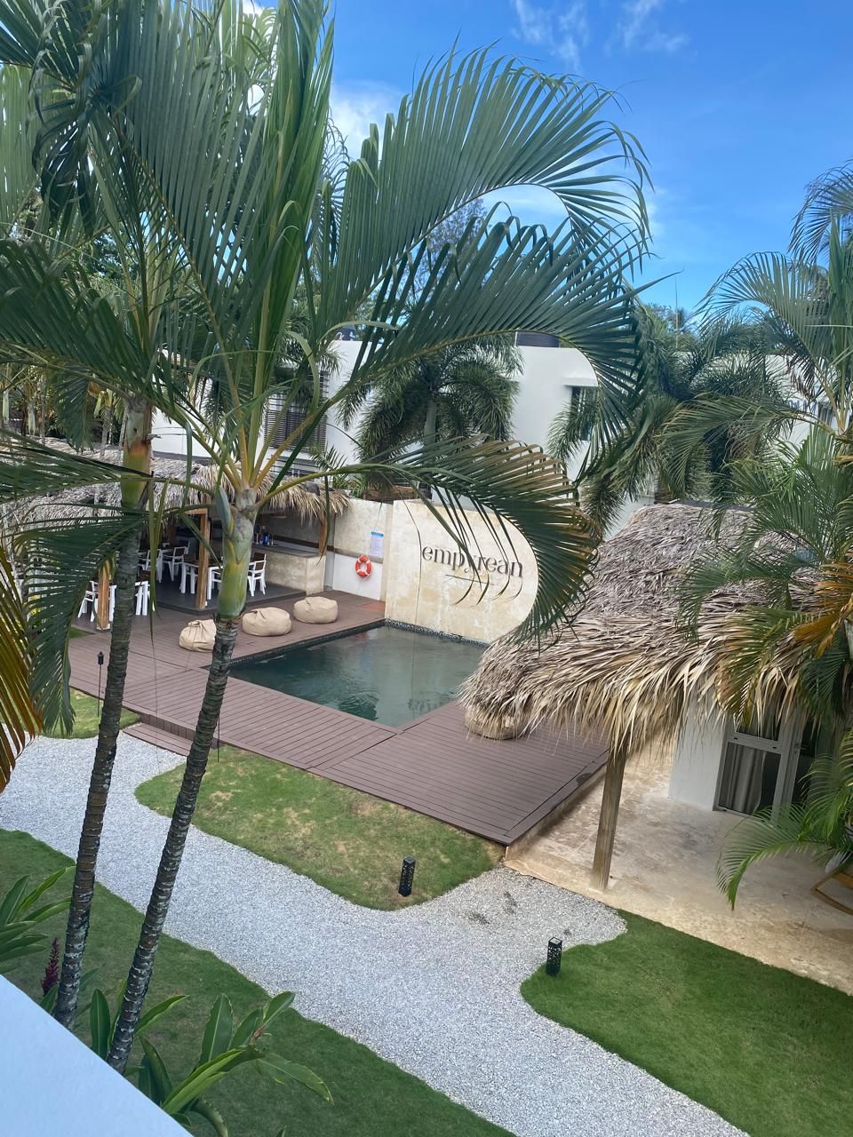 Zona de piscina amb palmeres, una estructura amb teulada de palla i un rètol que diu "empire".