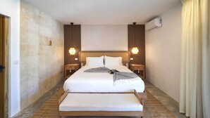 Une chambre d’hôtel avec un grand lit, deux tables de chevet, une tête de lit, un climatiseur fixé au mur et une fenêtre avec des rideaux.