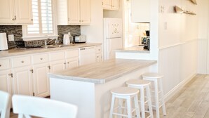 A modern kitchen with white cabinetry, a granite countertop, and a built-in island with bar stools. - Relaxing 3 bedroom cottage located in beautiful Prince Edward Island, Canada (Kensington)