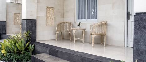 A modern hotel entrance with a stone facade, two wooden chairs, a small table, and steps leading to the entrance.