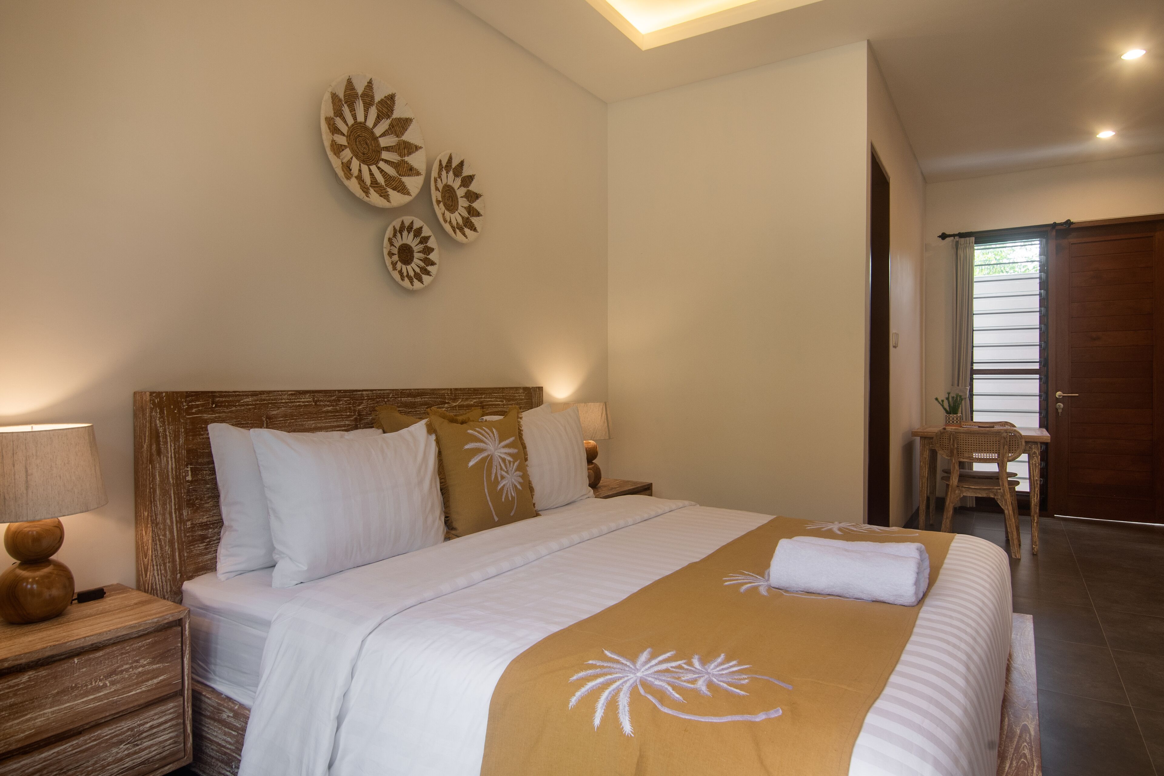 A neatly arranged bedroom with a large bed, a wooden nightstand with a lamp, and wall art.