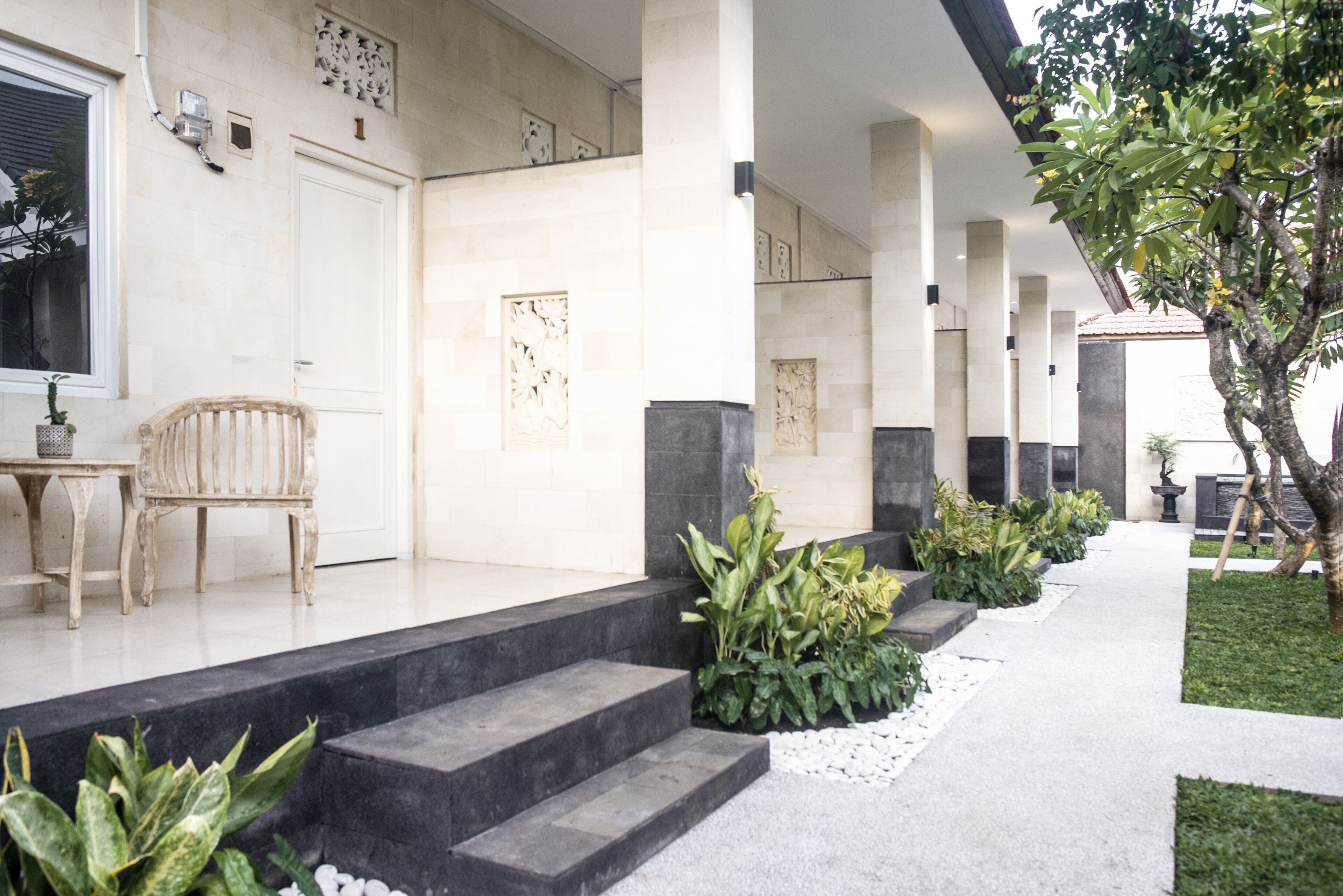 A modern building with a covered outdoor area, steps leading to a door, and a seating area with a chair and table.