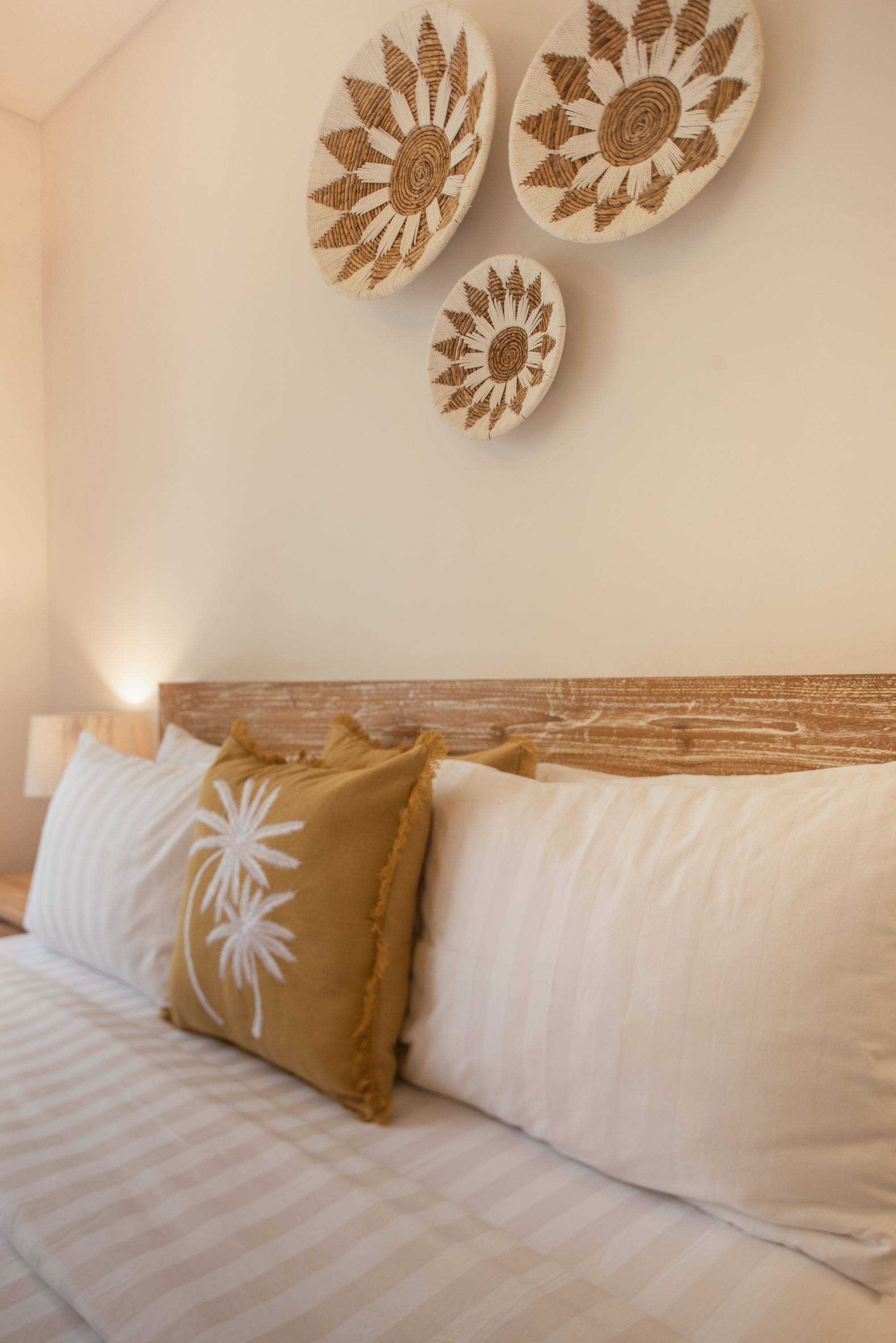 Una cama con ropa de cama blanca y cabecera de madera, acompañada de decoración en la pared con motivos de girasoles.