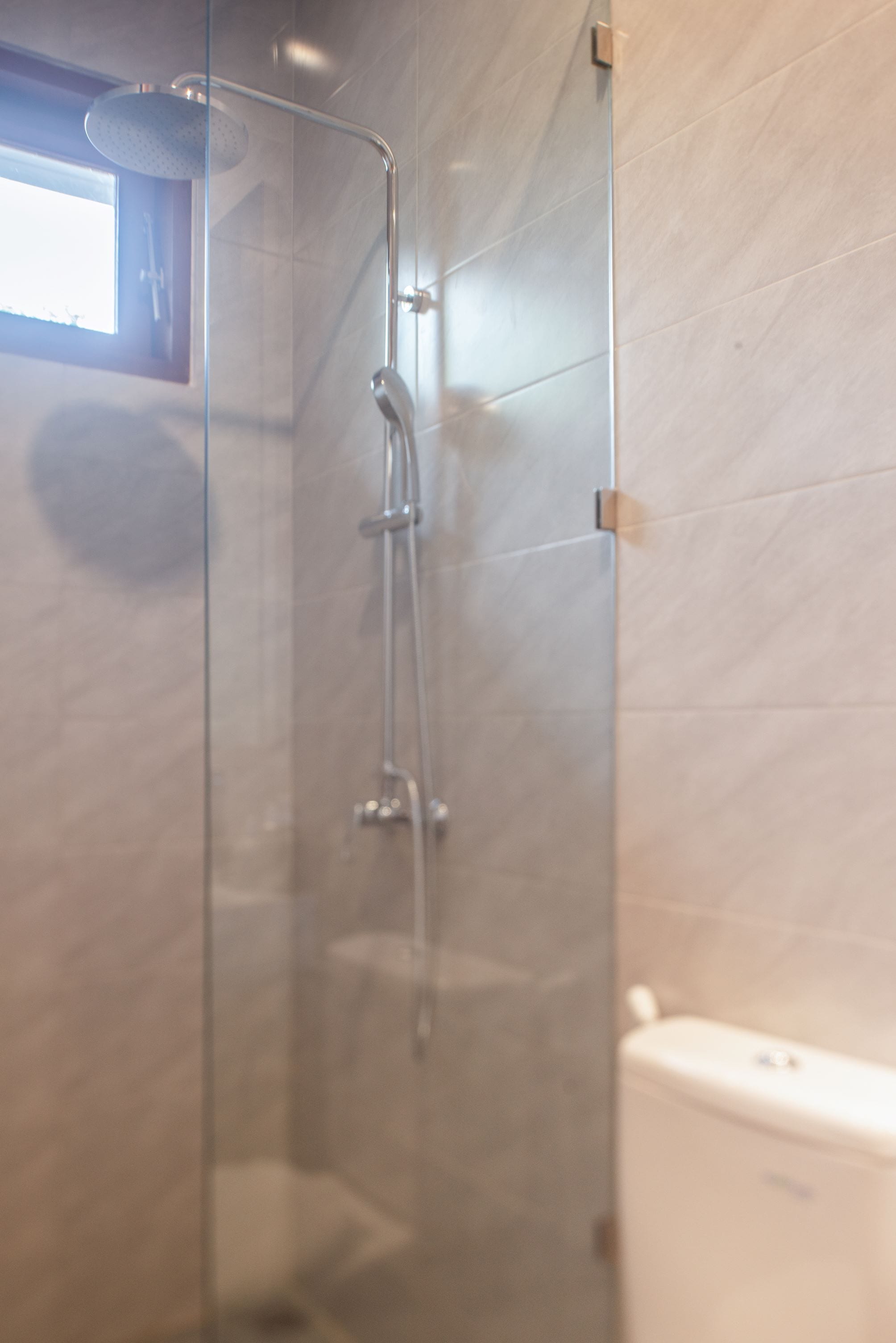 A glass-enclosed shower with a handheld showerhead and a wall-mounted faucet.