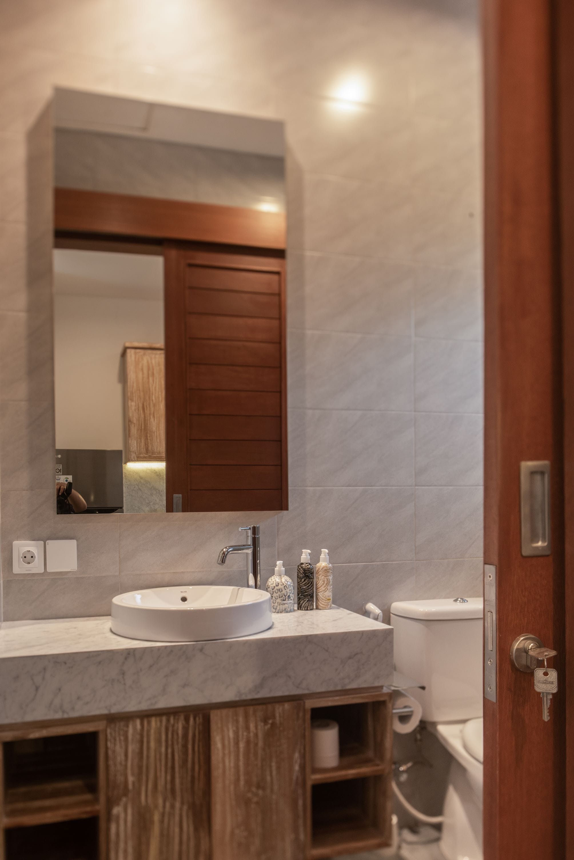 Une salle de bain avec un lavabo en marbre, des meubles en bois, un grand miroir et des toilettes.