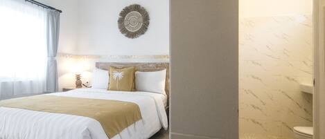 Una habitación de hotel con cama, mesita de noche, decoración en la pared y baño con inodoro y ducha.