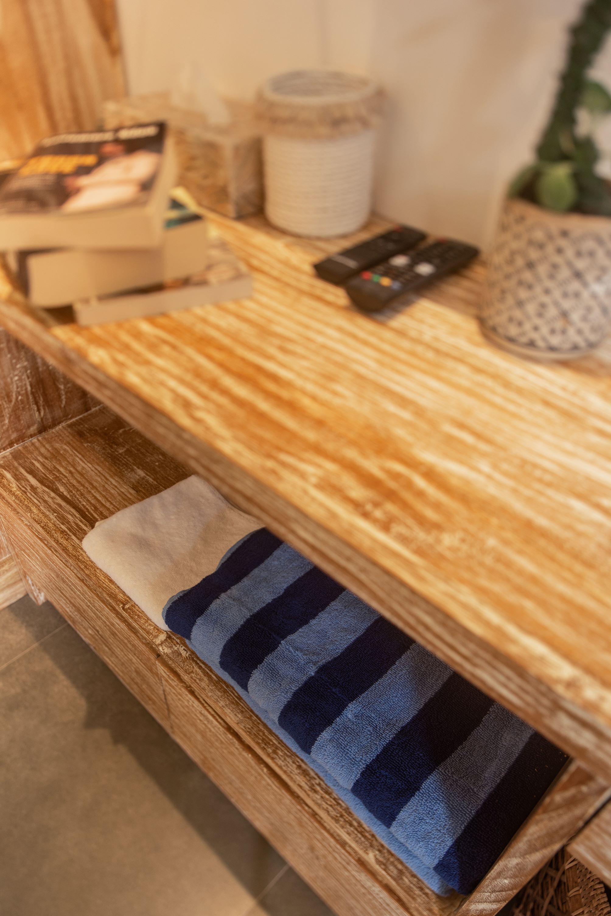 A wooden bench with a striped cushion, a remote control, and a book on the table.