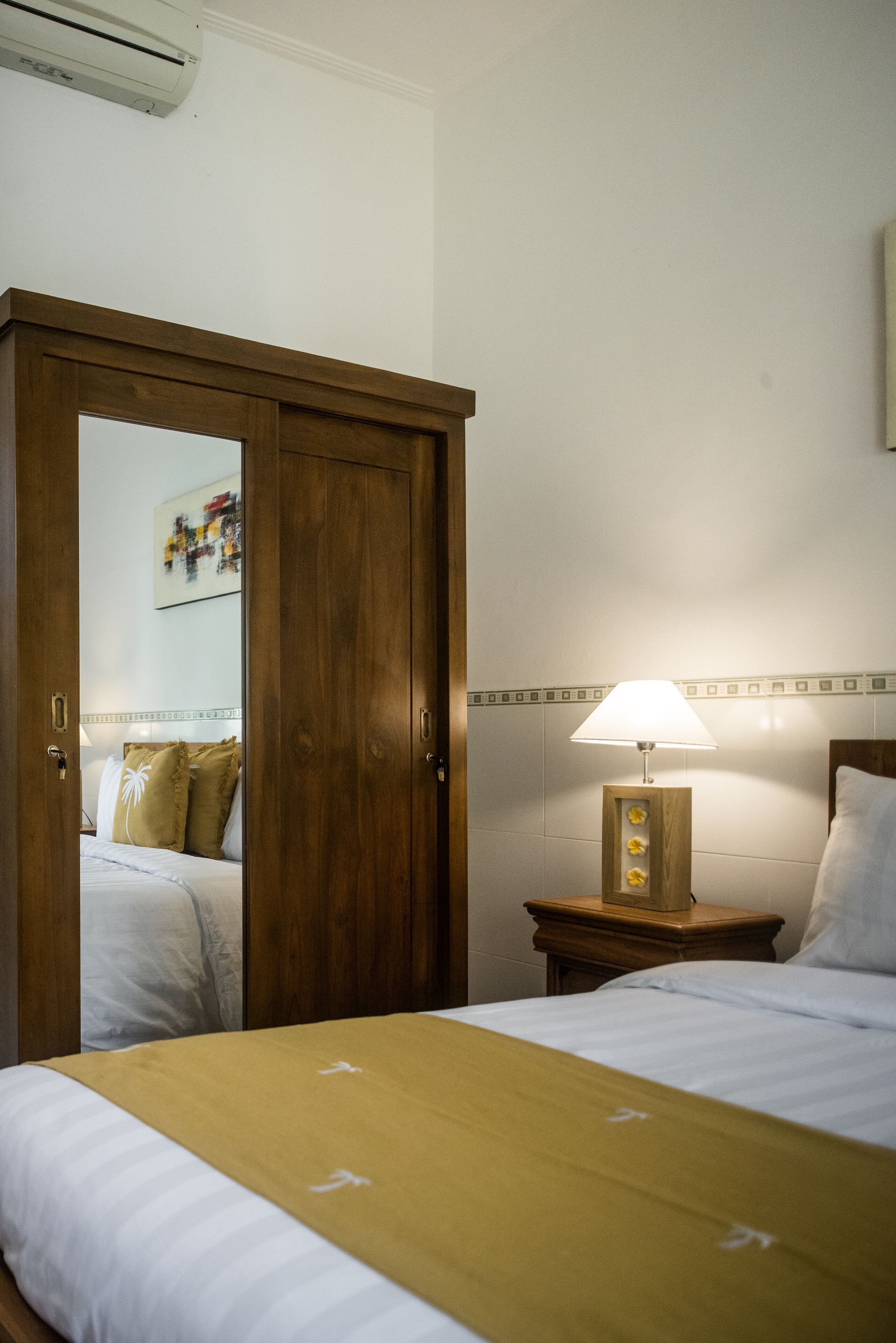 A hotel room with a bed, a nightstand with a lamp, and a wooden wardrobe.