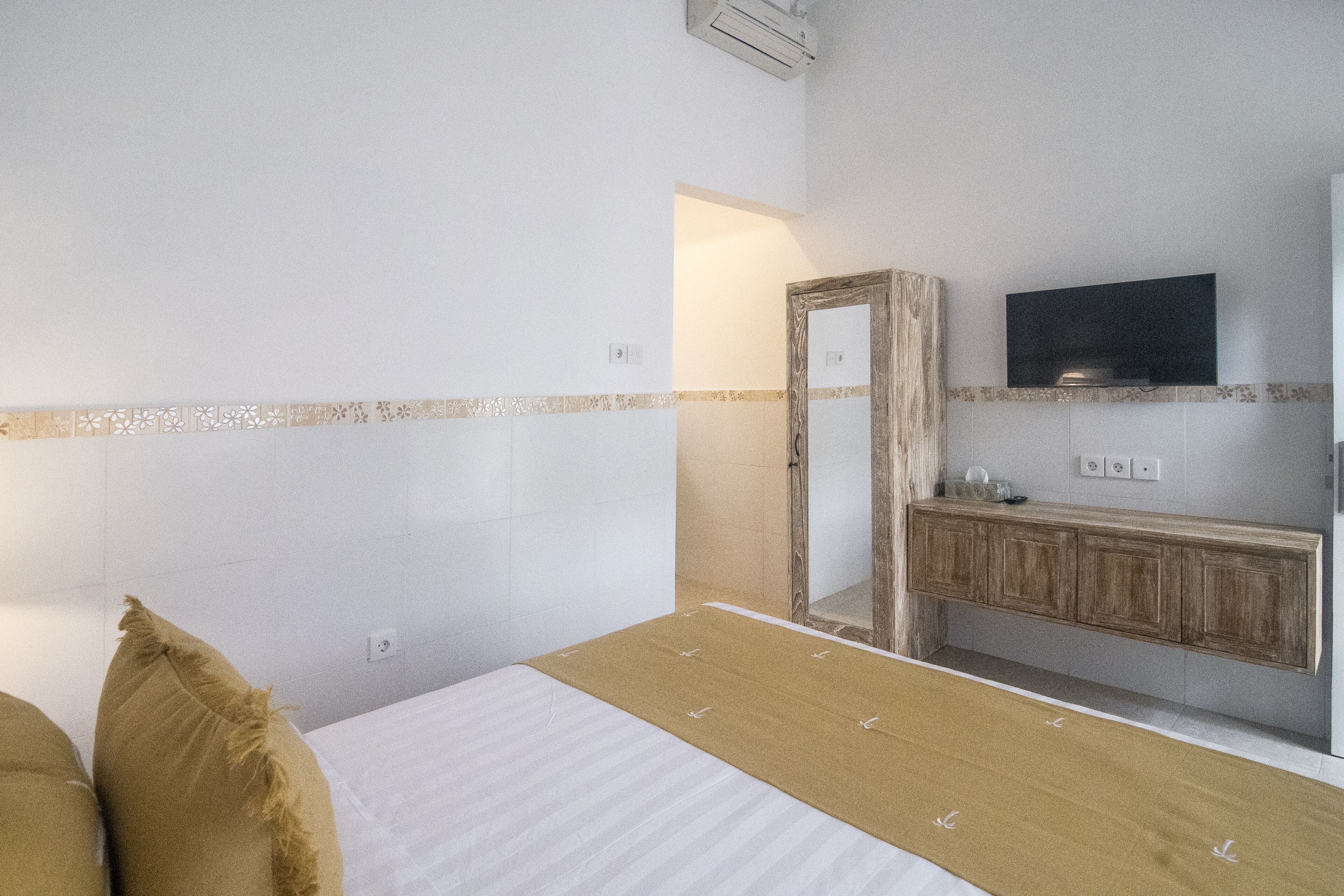 A bedroom with a bed, a wooden dresser, a mirror, and a television mounted on the wall.