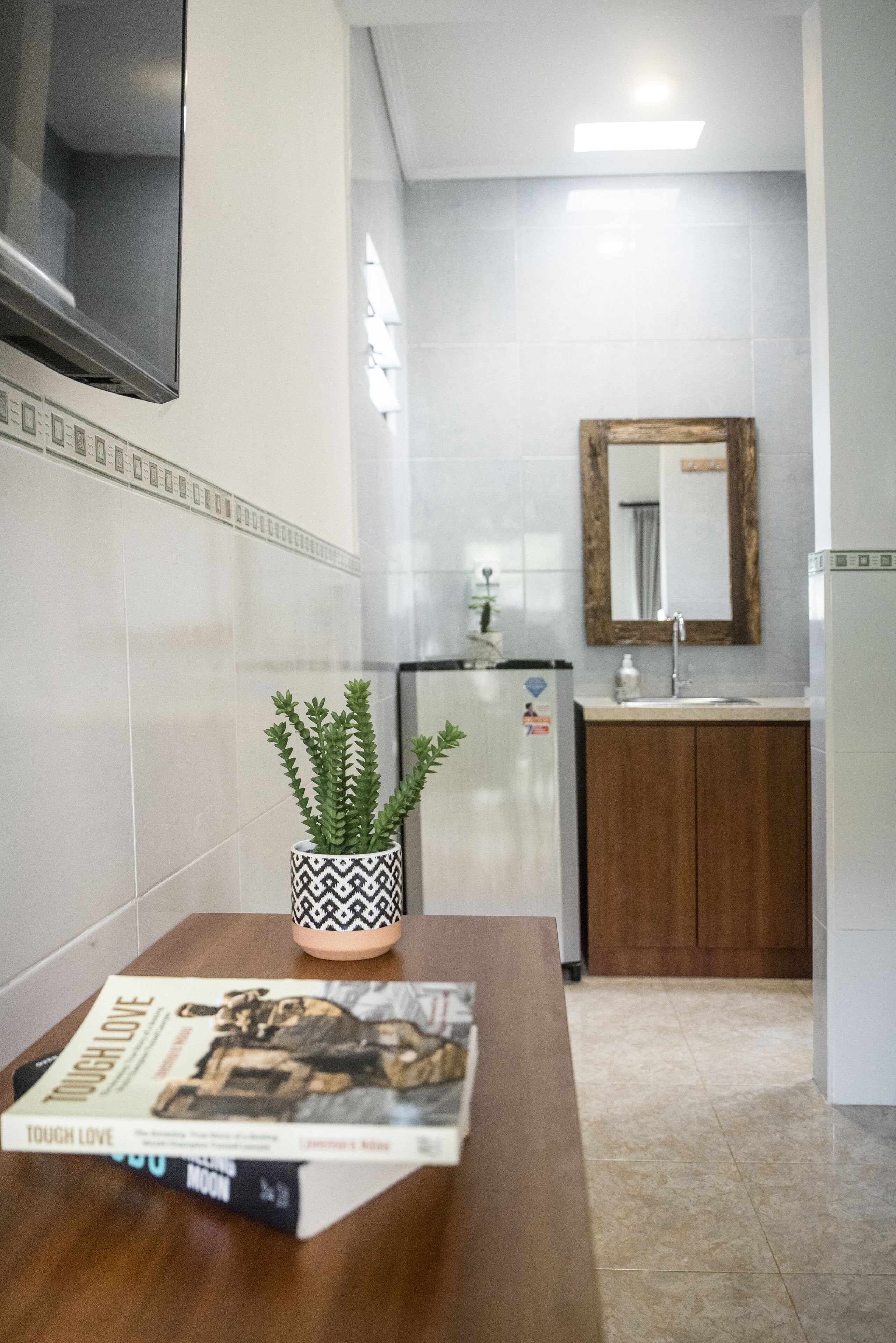 A modern kitchen with white tiles, a wooden cabinet, a sink, and a refrigerator.