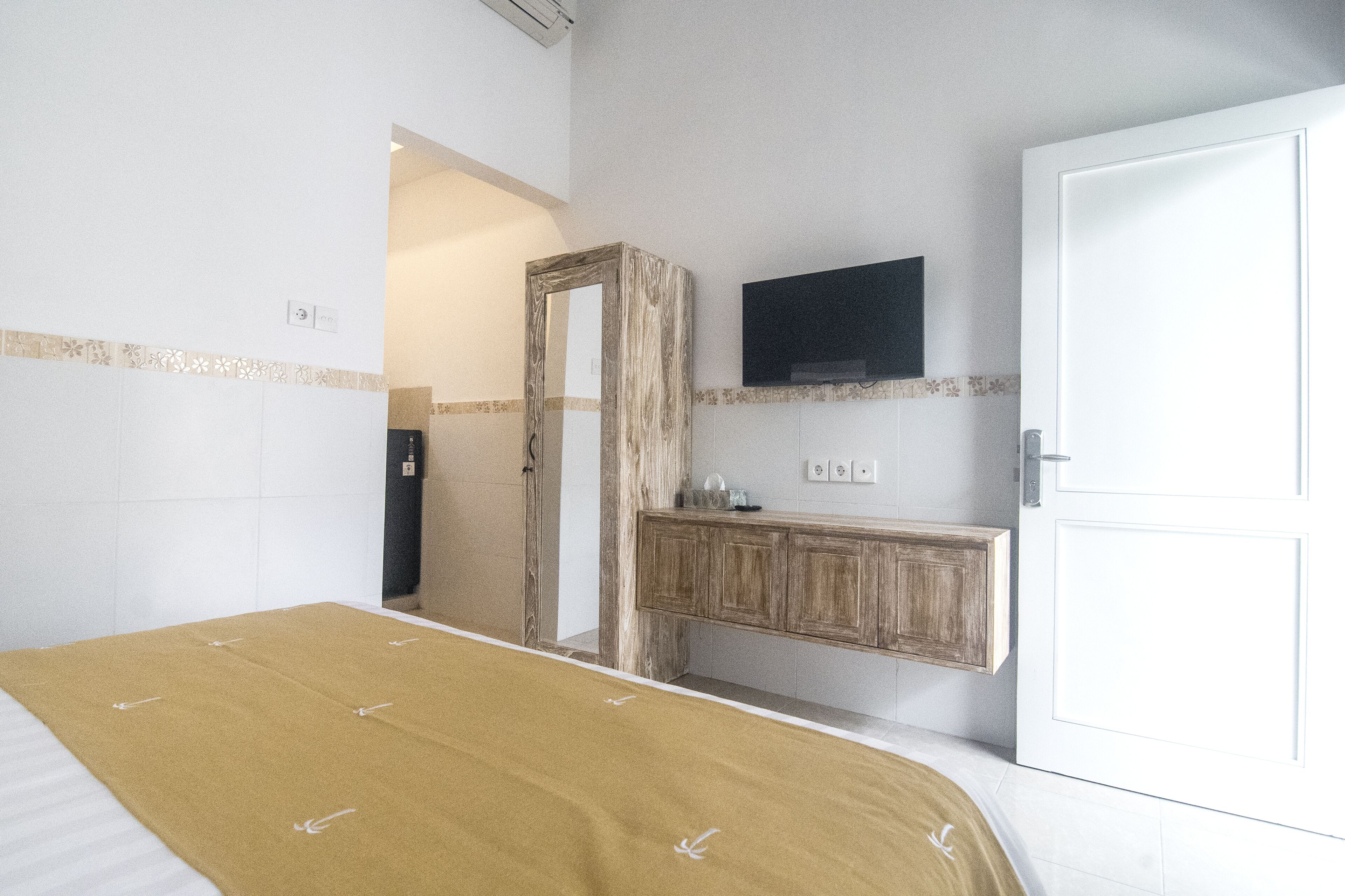 A hotel room with a bed, a wooden dresser, a television mounted on the wall, and a door.