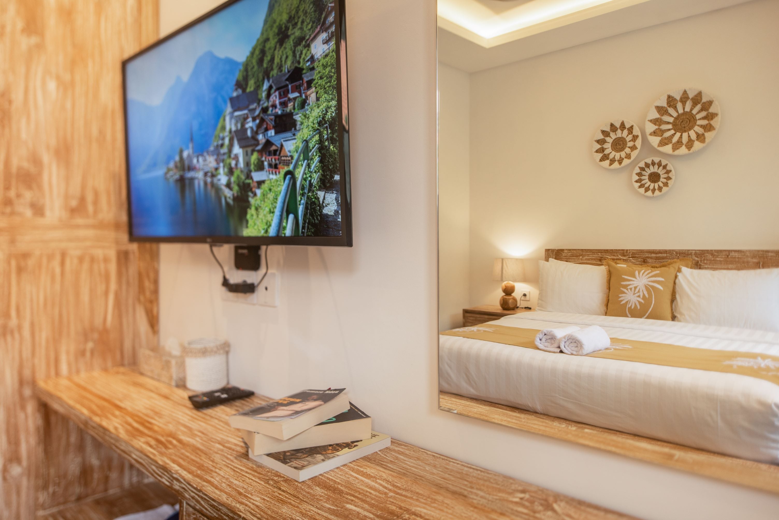 A hotel room with a bed, a bedside table with books, a TV mounted on the wall, and decorative wall art.