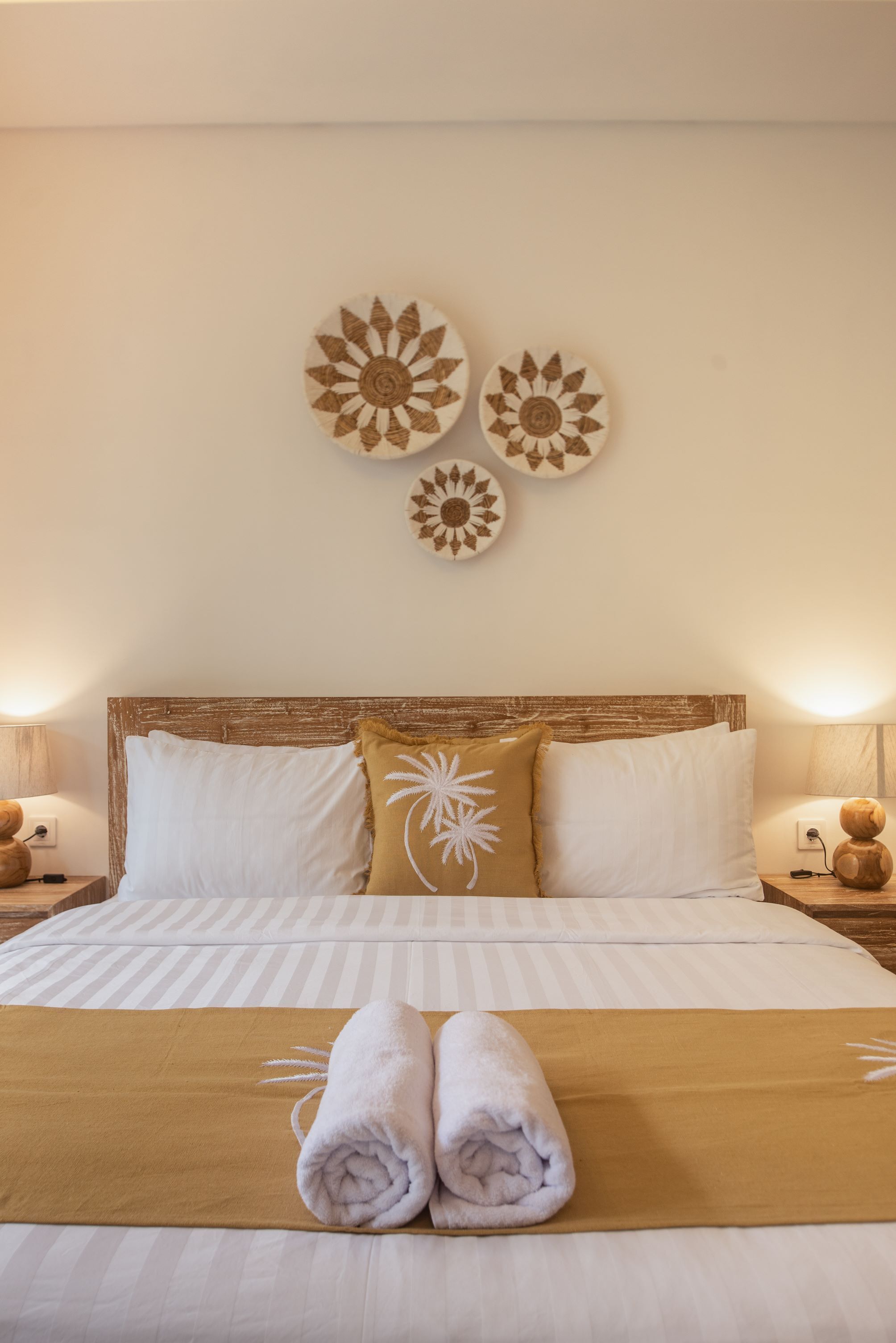 A neatly made bed with white and brown bedding, two decorative wall pieces, and a nightstand with a lamp.