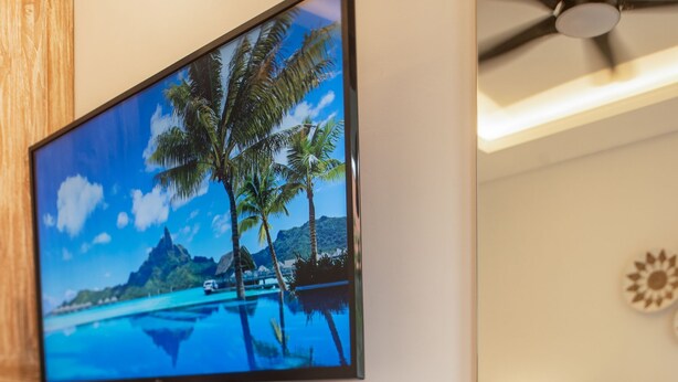 Un televisor de pantalla plana instalado en una pared de madera, mostrando una escena de playa tropical.