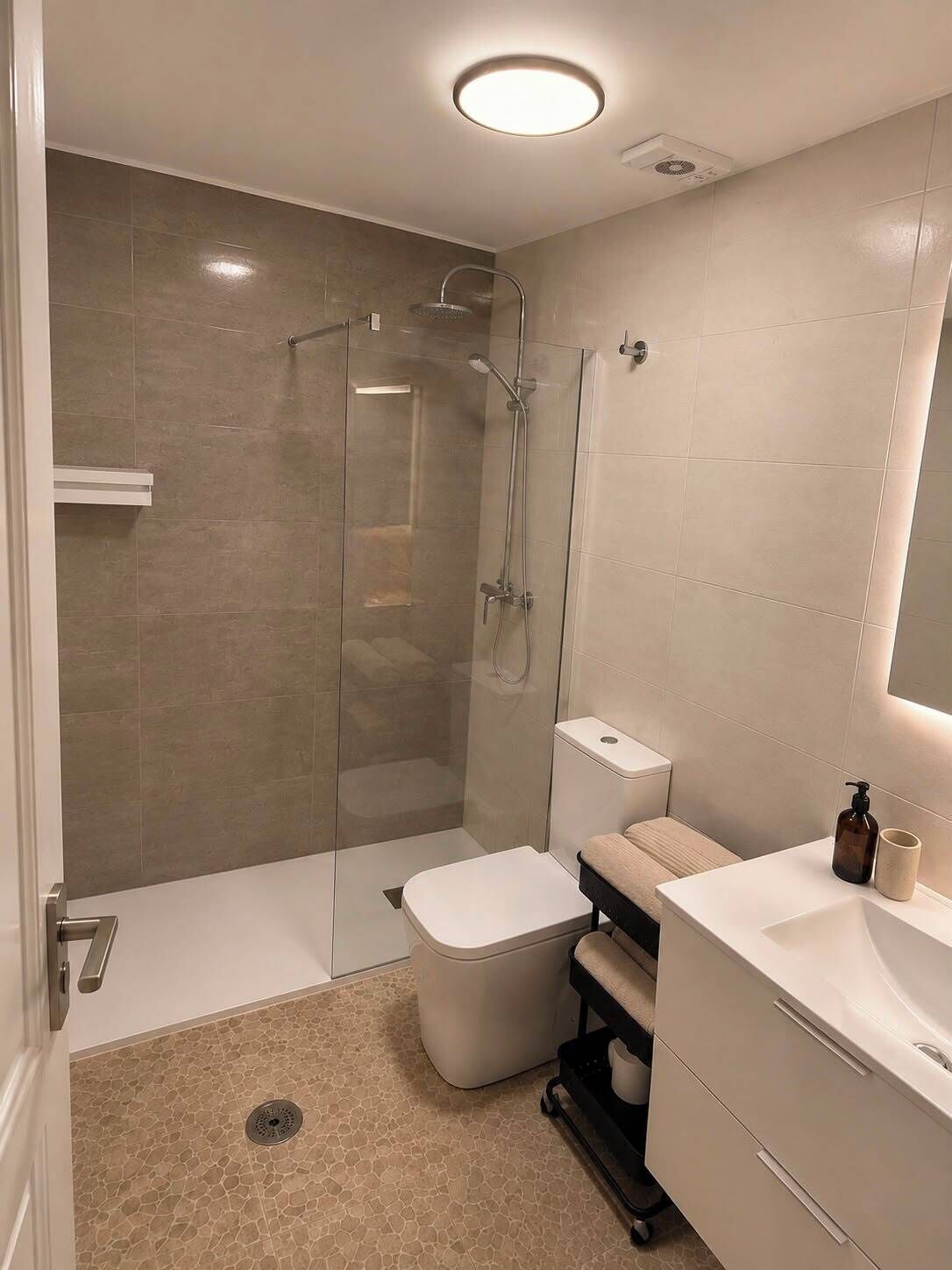 Un baño moderno con ducha de vidrio, inodoro y tocador con espejo.
