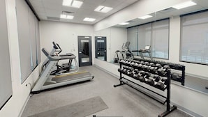 Ett gym med löpband, crosstrainer och ett ställ med hantlar.
