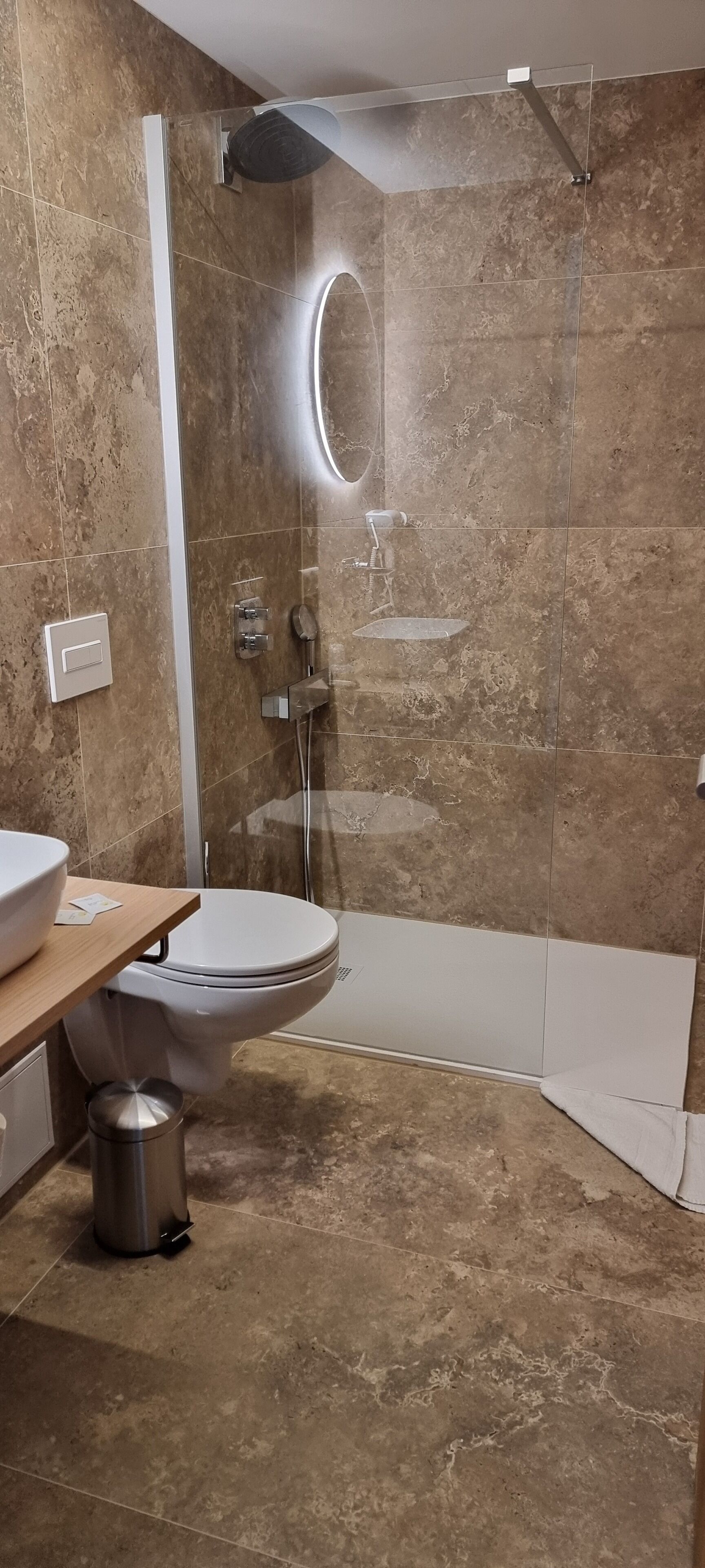 A modern bathroom with a glass-enclosed shower, a toilet, a sink, and a trash bin.