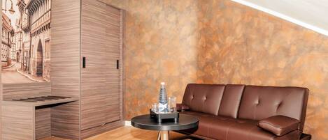 A modern room with a brown leather sofa, a round table with a bottle and glasses, and a wooden cabinet.