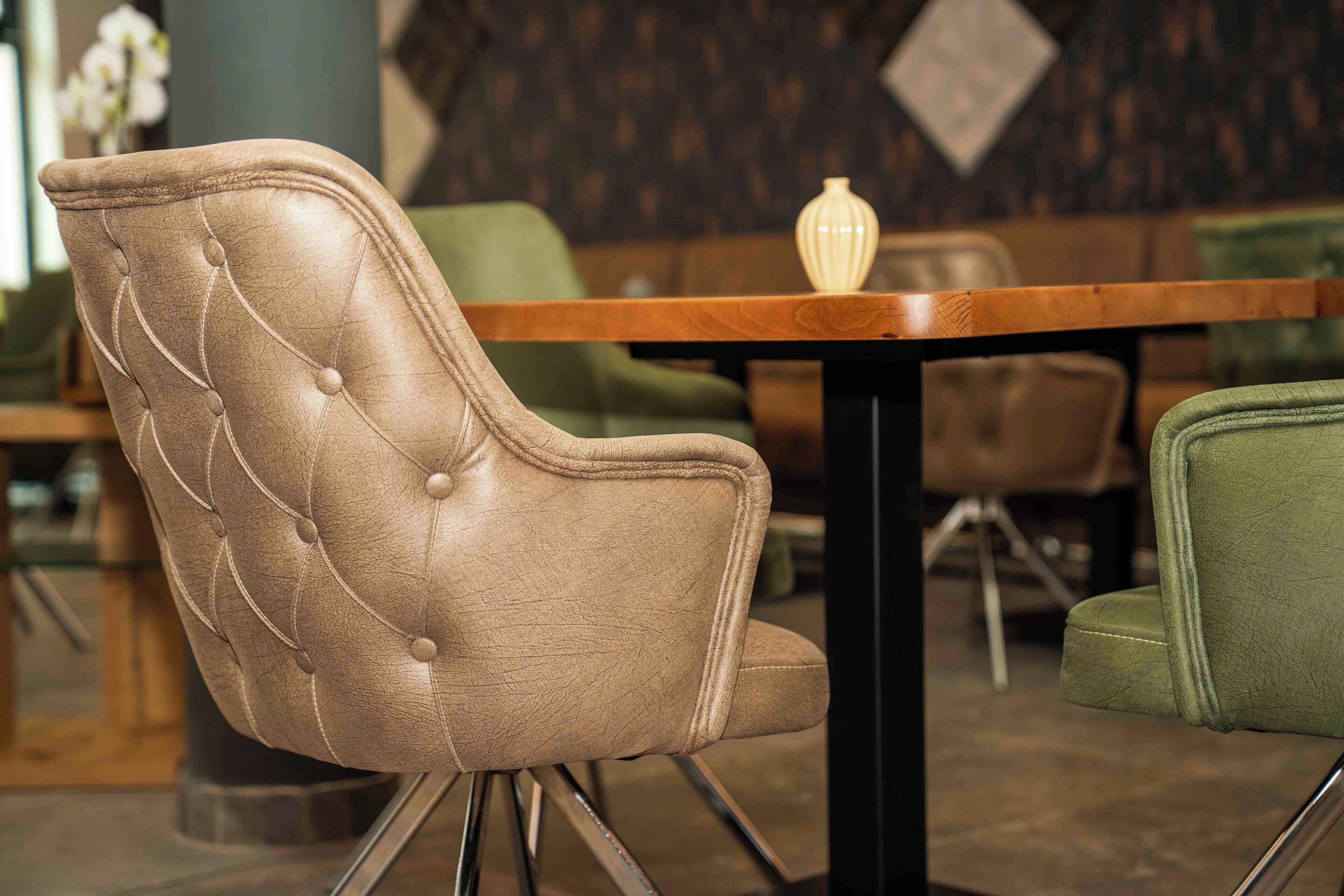 Un fauteuil en cuir marron, doté d’un dossier capitonné et de pieds en métal, placé devant une table en bois dans un restaurant.