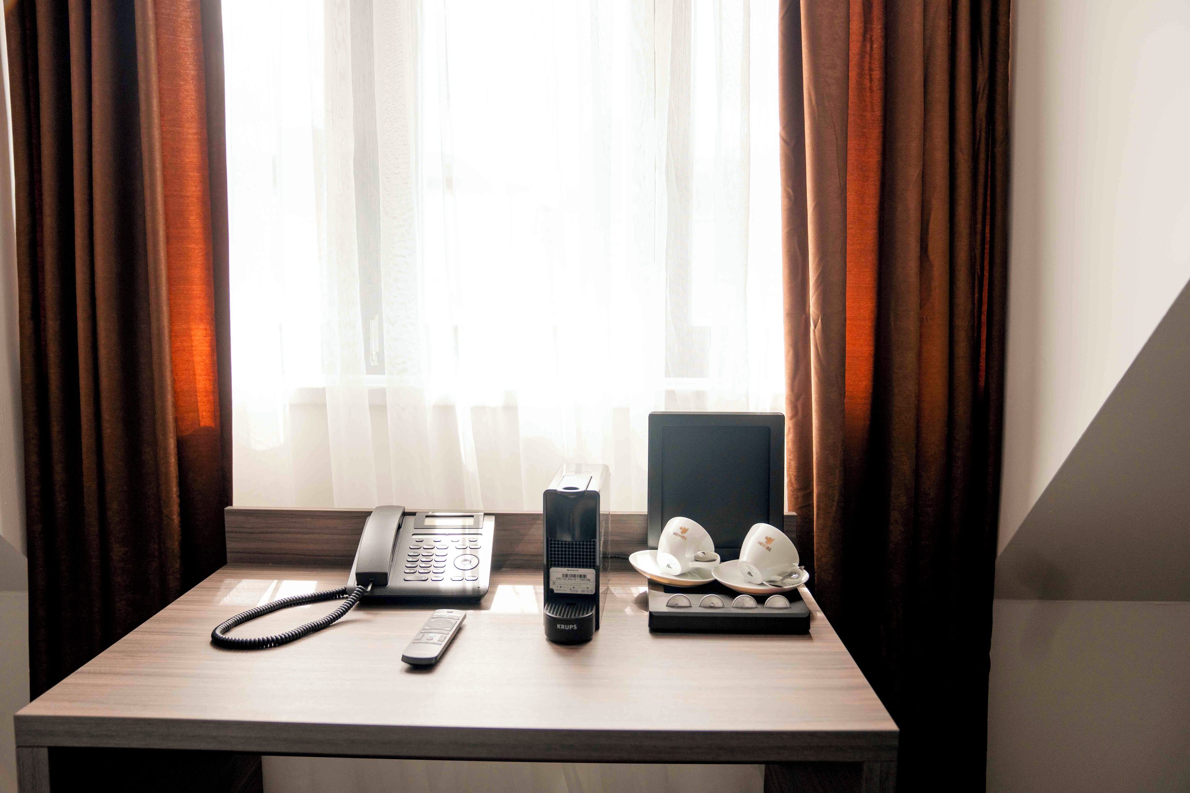 Un bureau dans une chambre d’hôtel, avec un téléphone, une télécommande et une paire de casques de chantier blancs.