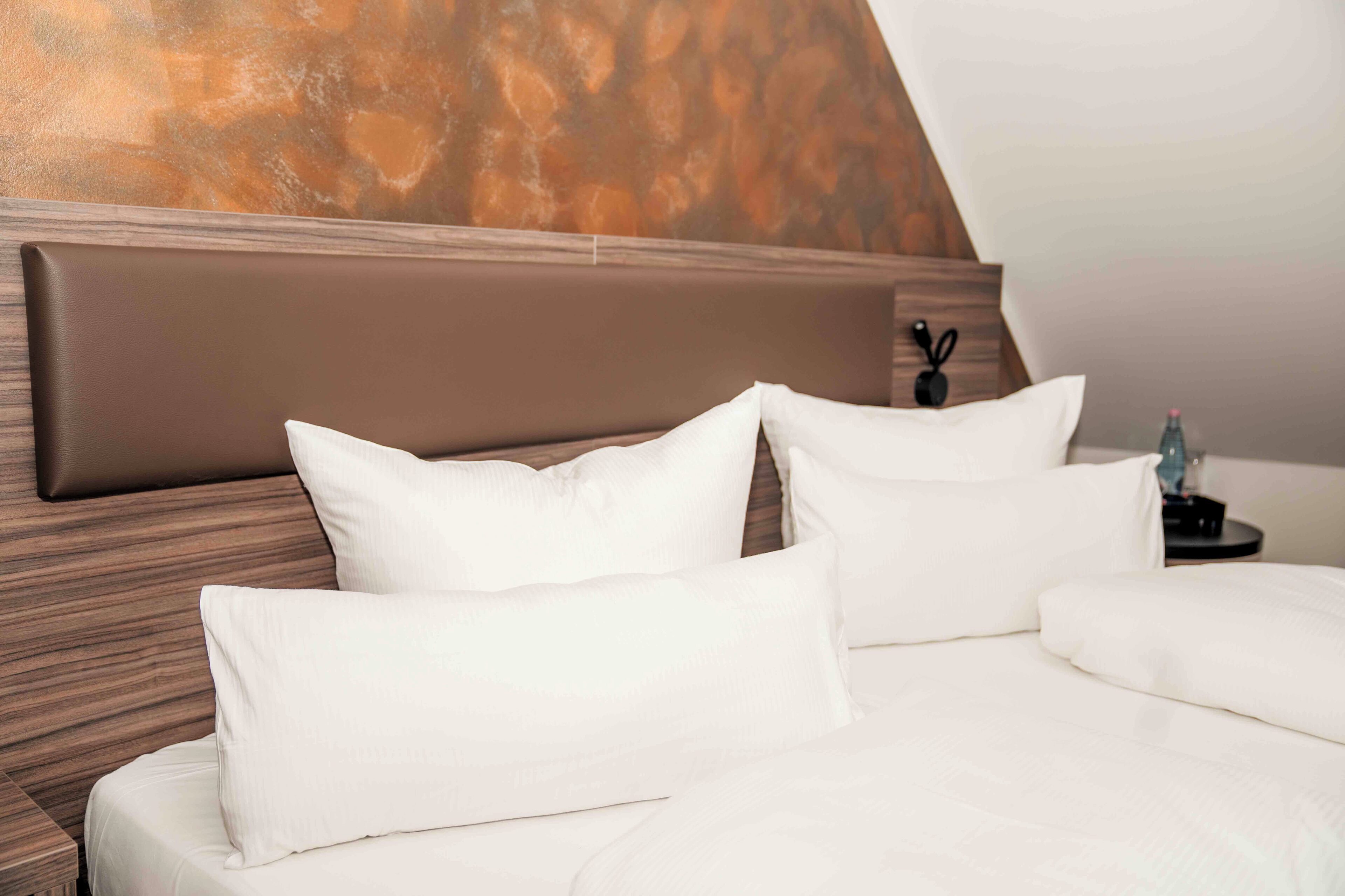 A neatly made bed with white linens and a wooden headboard.