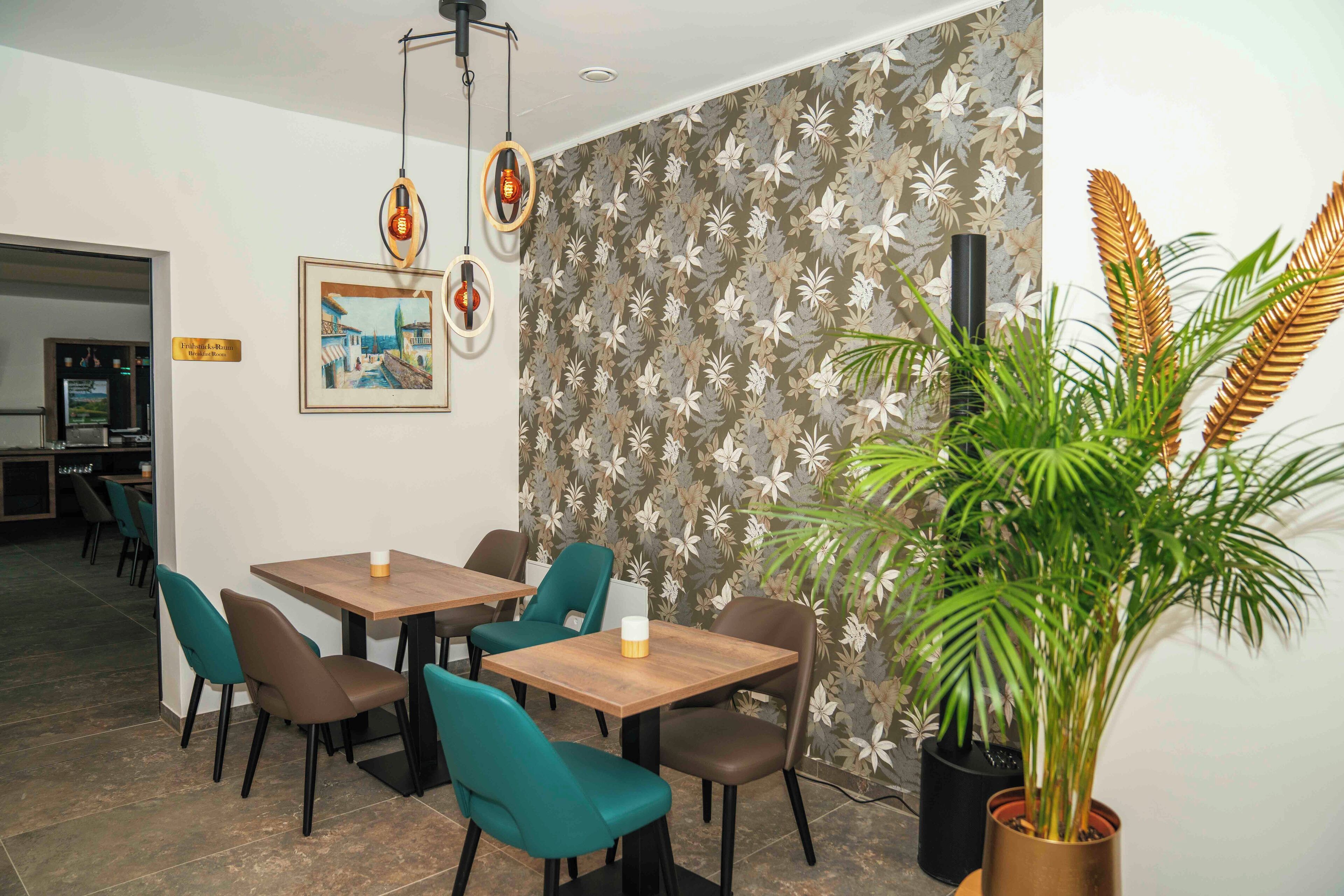 A dining area with tables and chairs, a potted plant, and a wall with a floral pattern.