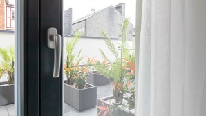 Een zicht door een deur op een binnentuin met plantenpotten en een gebouw op de achtergrond.