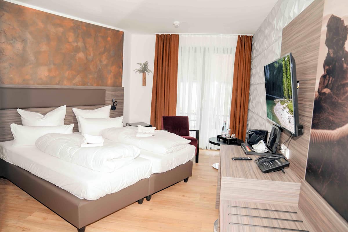 A hotel room with a large bed, a desk with a computer, a TV, and a window with curtains.