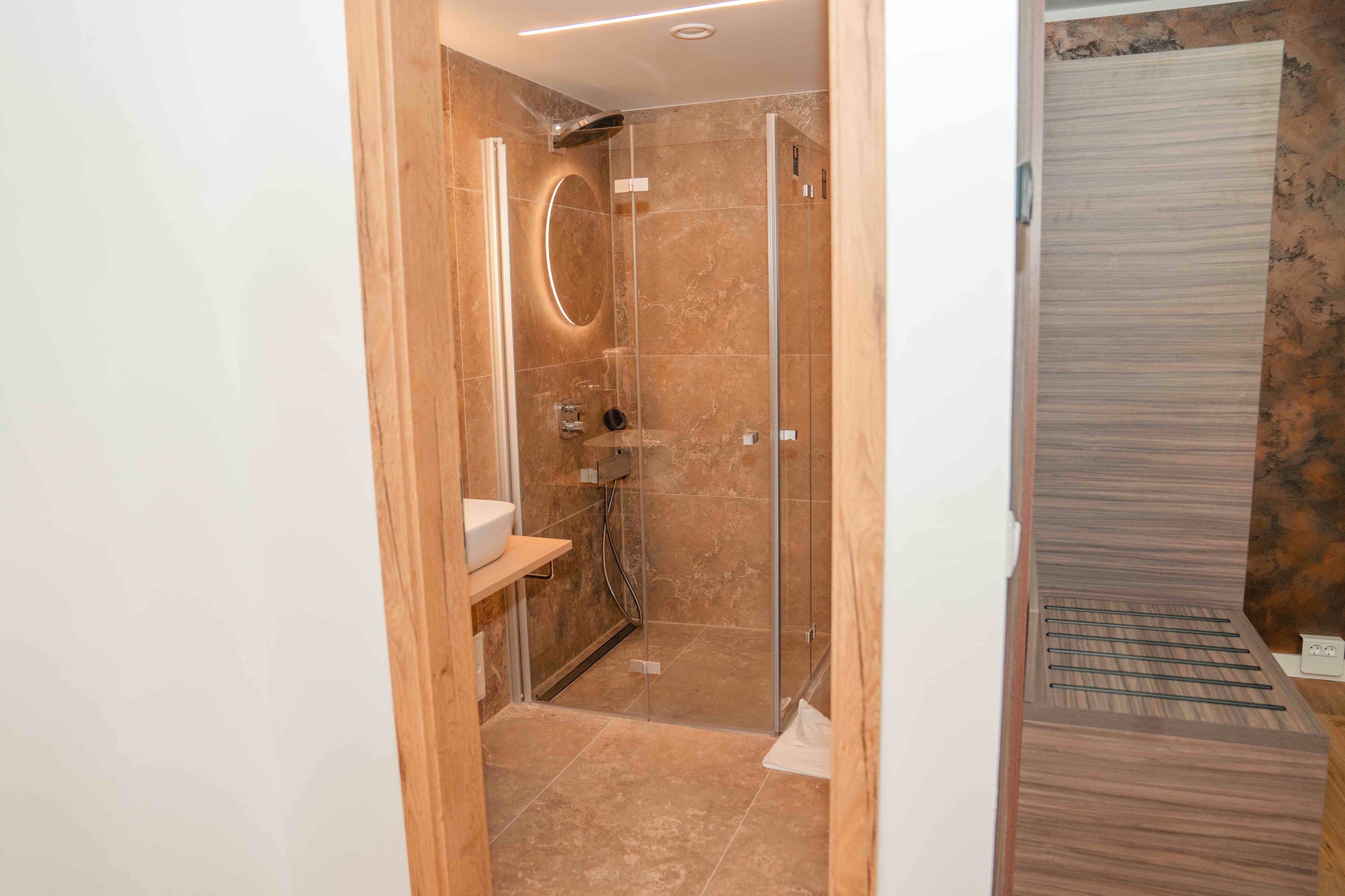 A modern bathroom with a glass shower enclosure, a wooden vanity, and a marble-tiled shower area.