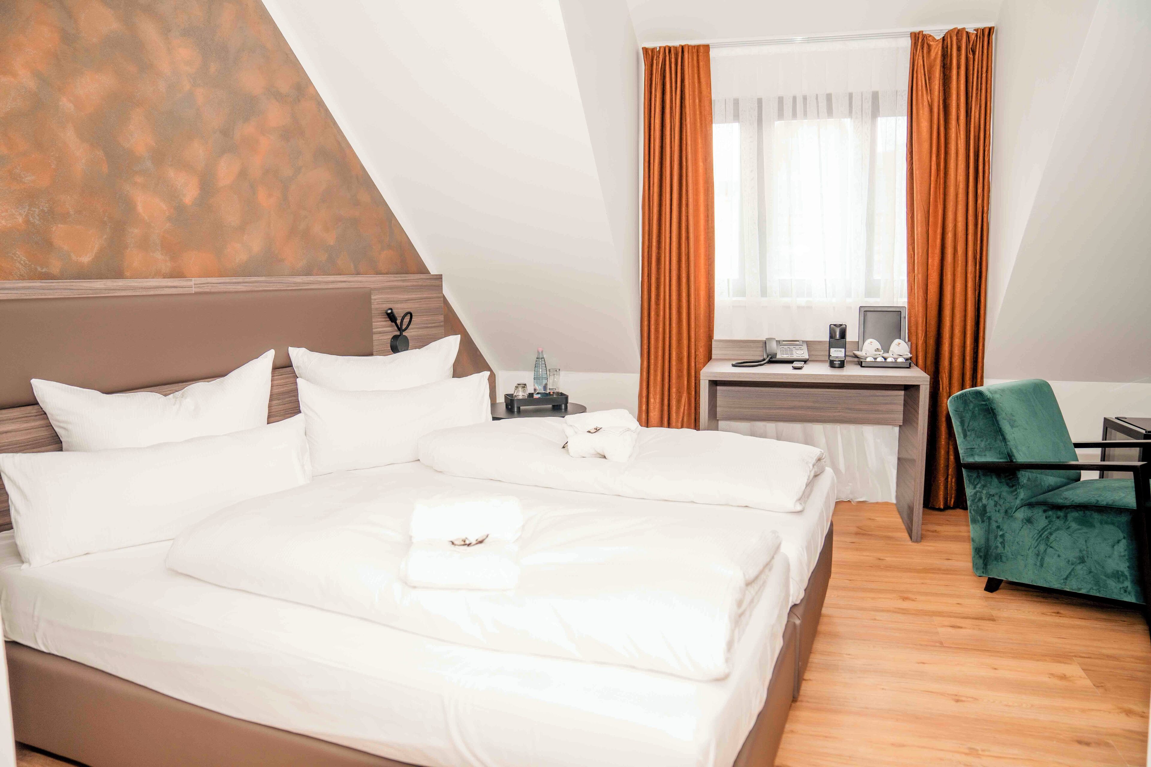 A hotel room with a large bed, a desk with a computer, and a green chair.