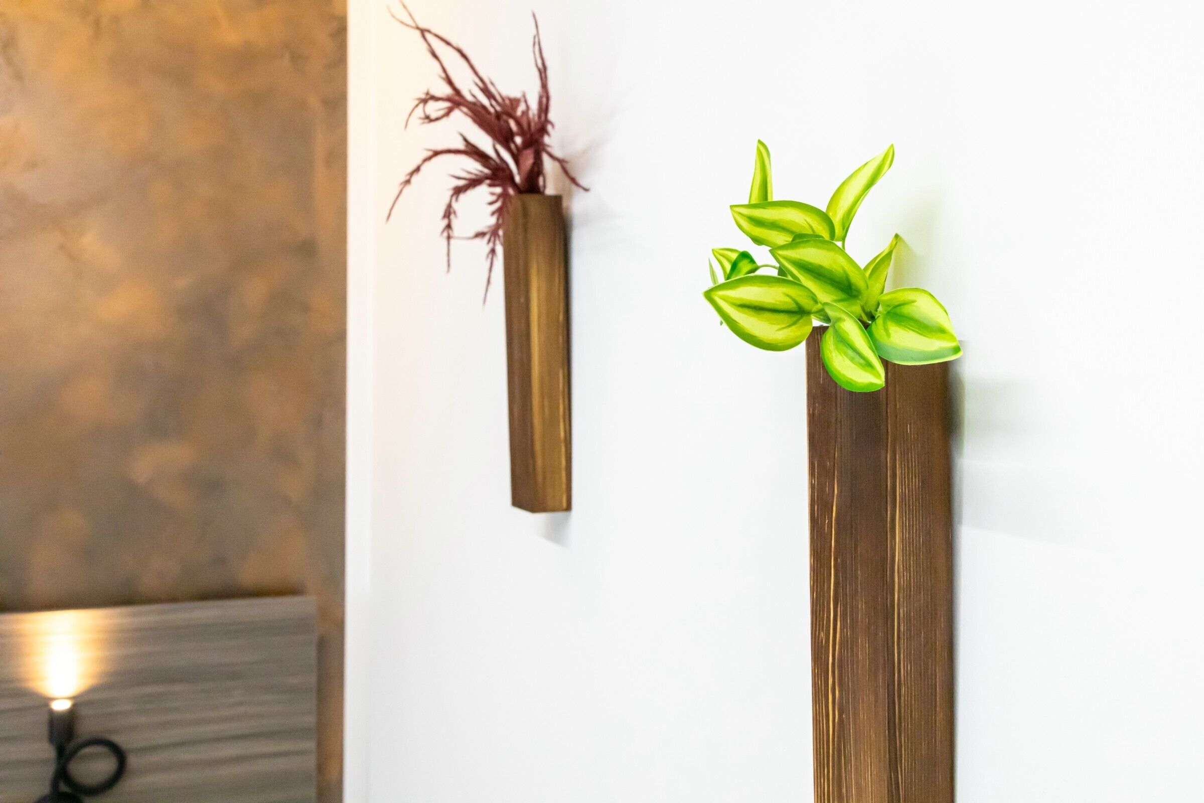 Two vertical wooden planters with plants against a white wall.