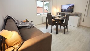 Un espai vital reduït amb sofà, taula de dinar, cadires, televisió i finestra que mostra un edifici.