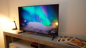 Televisor de pantalla plana sobre un suport de fusta, amb un cel nocturn projectat, una làmpada i revistes.