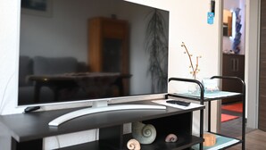 Una sala de estar moderna con un televisor de pantalla plana, un mueble de madera, una planta y una pequeña mesa con un jarrón.