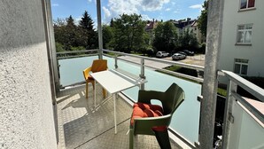 Un balcón con mesa y sillas, una piscina y vistas a coches aparcados y edificios.