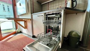 Una cocina con lavavajillas, una ventana que da a edificios y una alfombra roja.
