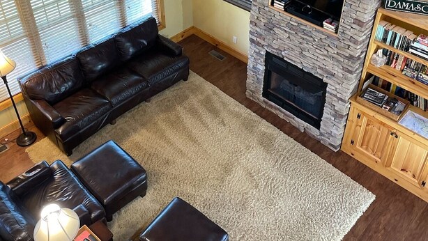 A cozy living room with a stone fireplace, leather furniture, and a ceiling fan.