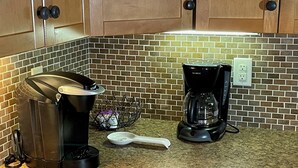 A kitchen with a coffee maker, a spoon, and a basket on the counter.