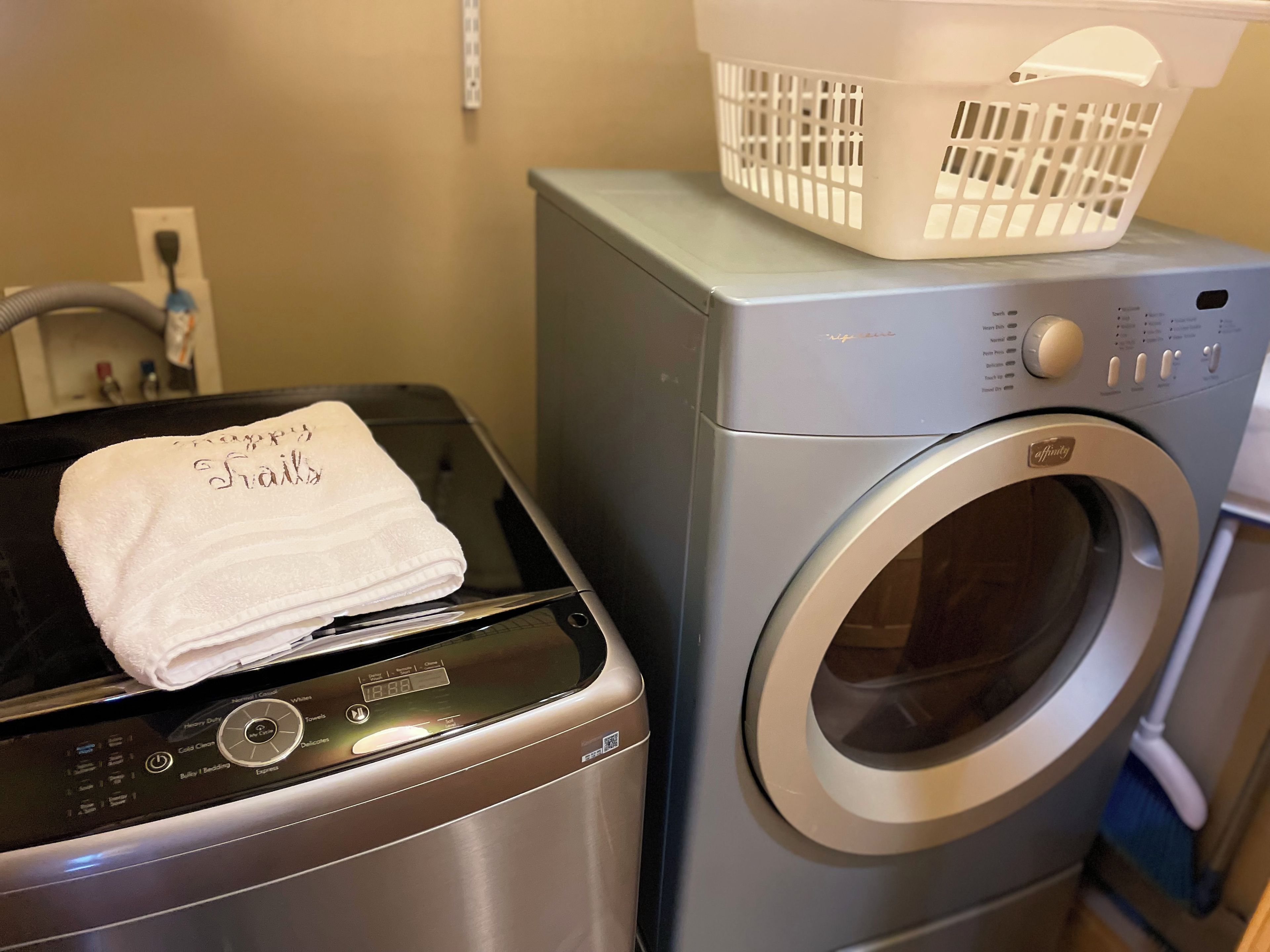 A front-loading washing machine with a basket on top, a dryer, and a folded towel with text on it.