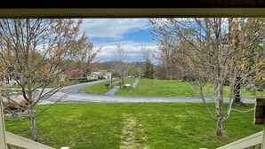 A view from a porch overlooking a grassy area with a pathway leading to a road.