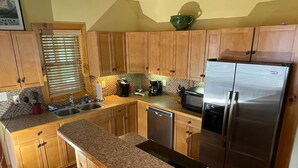 A kitchen with wooden cabinets, granite countertops, a stainless steel refrigerator, and a dishwasher.