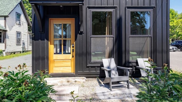 Il s’agit d’un bâtiment moderne doté d’une porte en bois et de deux fenêtres. On peut y voir deux chaises à l’extérieur.