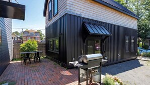 Une maison moderne avec une façade noire, une terrasse en briques et un barbecue.