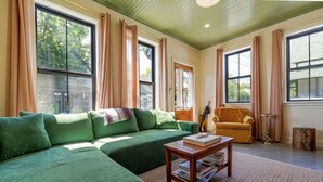 Un salon chaleureux avec un canapé d’angle vert, un fauteuil jaune et une table basse en bois sur laquelle sont posés des livres.