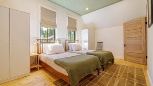 Une chambre avec deux lits, une armoire en bois, une fenêtre avec des stores et une porte.